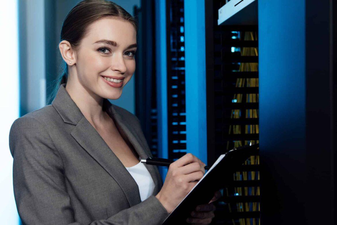 cheerful businesswoman writing while holding clipboard in server room programmatrice sorridente