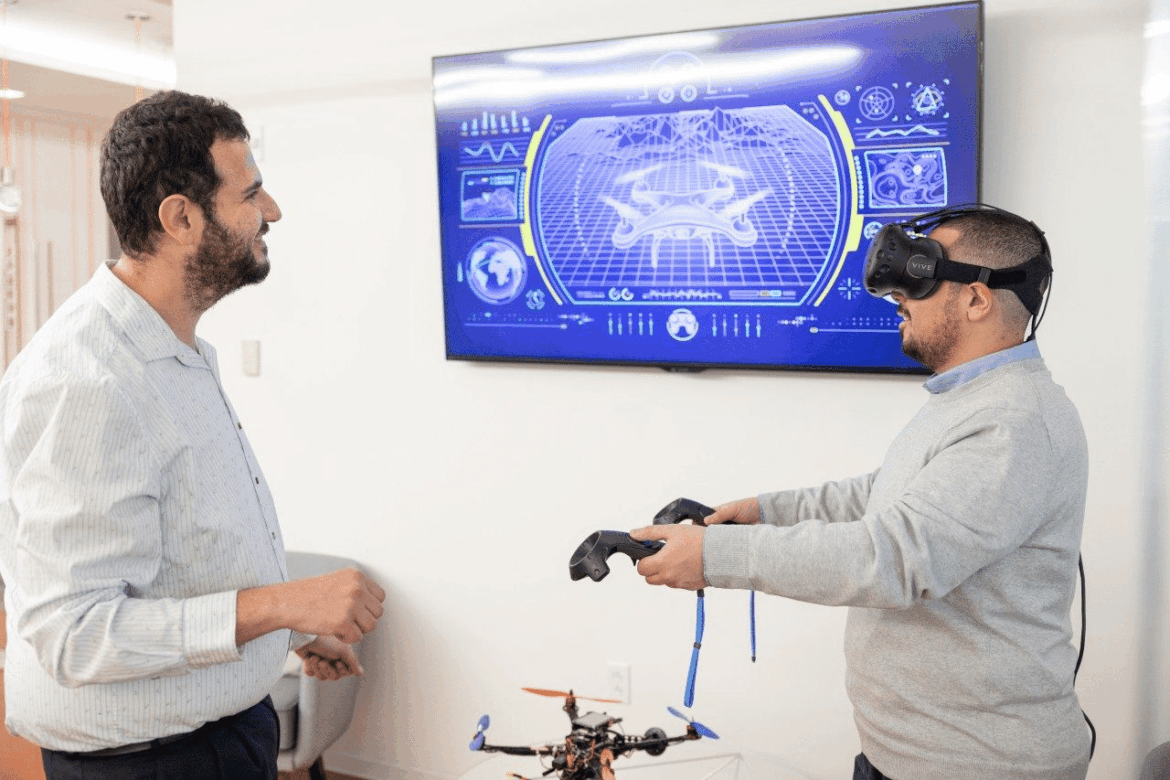 (Da sinistra) Walid Saad e lo studente di dottorato Omar Hashash provano una cuffia per la realtà virtuale simile a quelle che spesso si usano per interagire con i gemelli digitali nel metaverso. Foto di Chelsea Seeber per Virginia Tech.